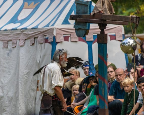 Ein Mann in der Renaissancekleidung führt eine Show vor einem Publikum mit Kindern und Erwachsenen.