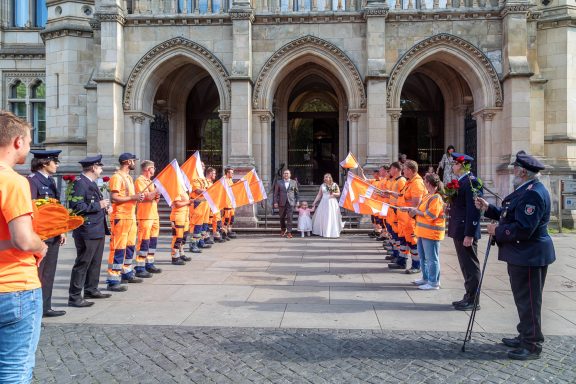 Menschen in Uniformen und Anzügen stehen in einer Reihe vor einem historischen Gebäude.