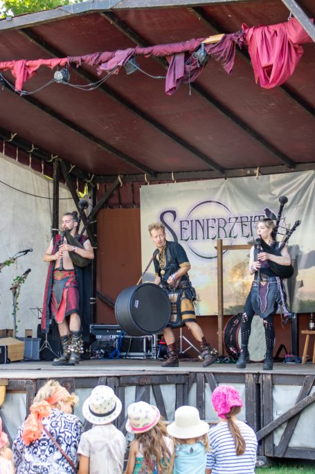 Drei Musiker in mittelalterlicher Kostümierung spielen auf einer Festivalbühne.