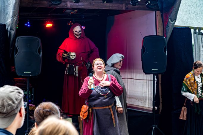 Zwei Darsteller in historischen Kostümen auf einer Bühne, Zuschauer im Vordergrund.