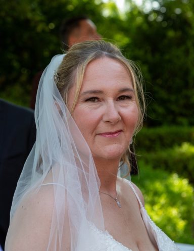 Frau mit Brautkleid und Brautschleier, lächelnd im Freien.