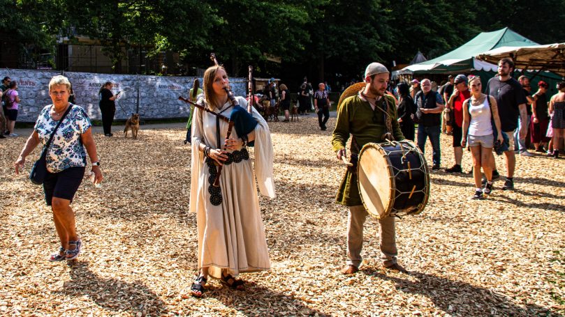 Leute in historischen Kostümen spielen Musik auf einem Festival mit Besuchern im Hintergrund.