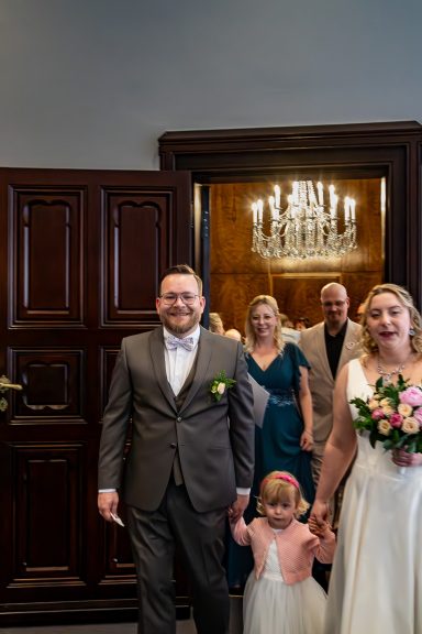 Brautpaar mit Blumen, Kind und Gästen in eleganter Hochzeitsatmosphäre.