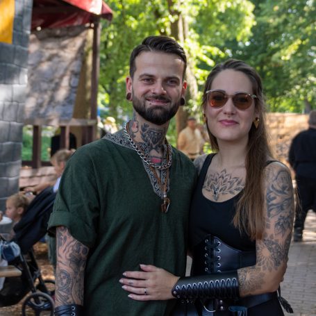 Paar mit Tätowierungen, lächeln und umarmen sich in einer natürlichen Umgebung.