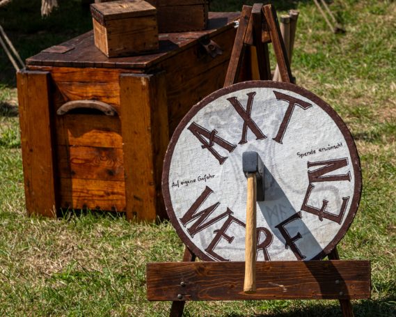Holzscheibe mit der Aufschrift "Axt werfen" und einer Axt, im Freien auf dem Gras.