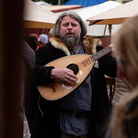 Mann mit einer Laute in historischer Kleidung bei einem Markt.