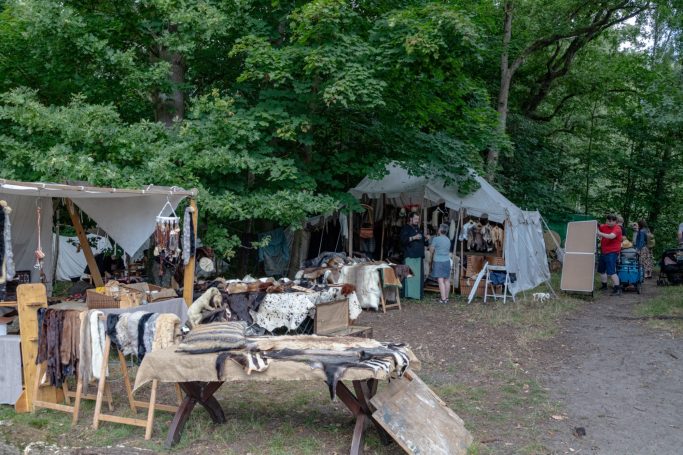 Markt mit Ständen und Zelten im Freien, umgeben von Bäumen. Handwerkswaren sind ausgestellt.