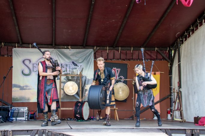 Drei Musiker in mittelalterlicher Kleidung spielen Musikinstrumente auf einer Bühne.