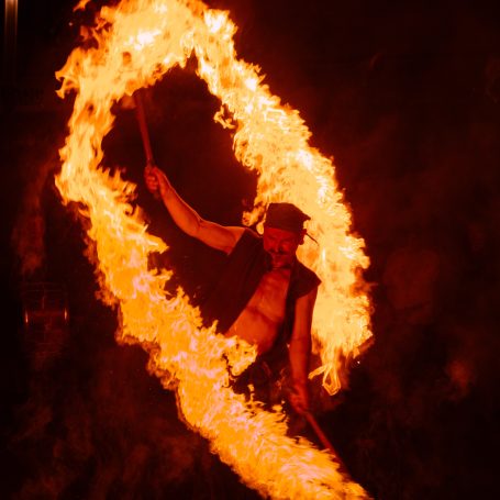 Feuerspucker tanzt mit brennendem Batons in einem leuchtenden Feuerring.