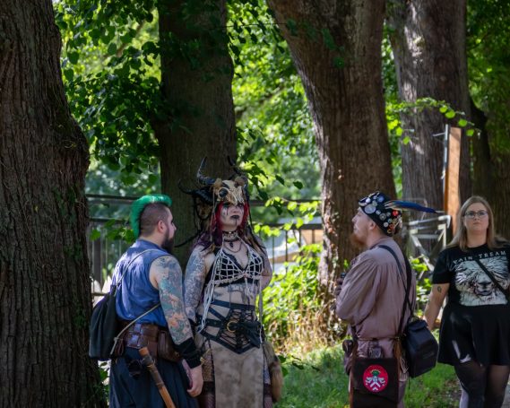 Gruppengespräch von vier Personen in fantasievoller Kleidung zwischen Bäumen.