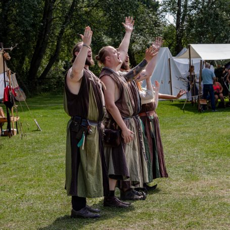 Männer in historischen Kostümen bei einem Fest, die fröhlich in die Luft weisen.