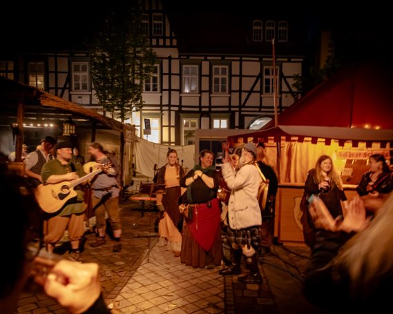 Mittelalterliches Fest mit Menschen in historischen Kostümen und Musik bei Nacht.