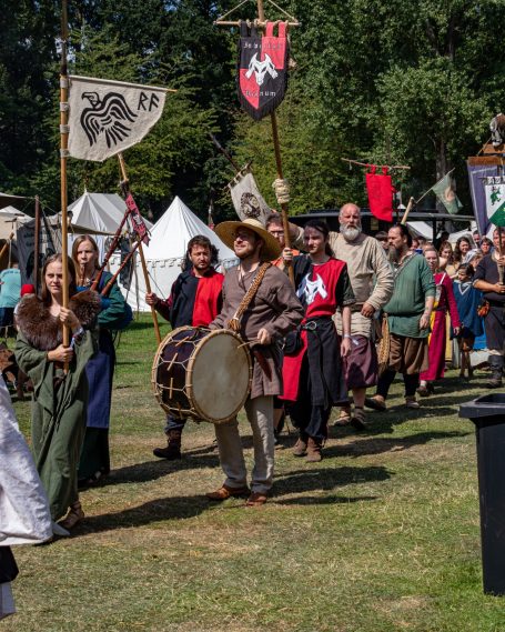Reenaktoren in historischen Kostümen marschieren mit Bannern und Trommel.