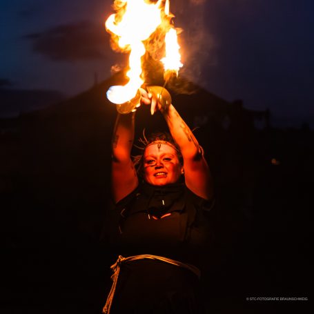 Frau führt eine Feuershow auf der Bühne bei Nacht durch.