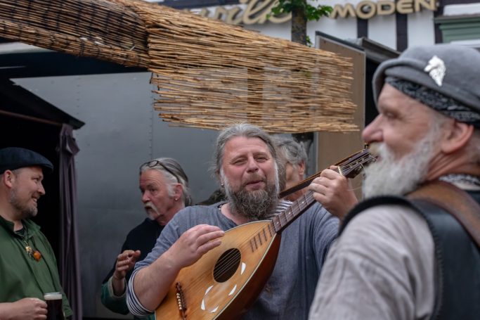 Männer in historischen Kostümen, die mit einer Laute und Gesang musizieren.