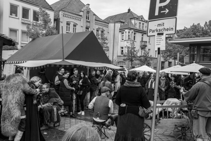 Menschenansammlung unter Zelten auf einer Straße, einige sitzen, andere unterhalten sich.