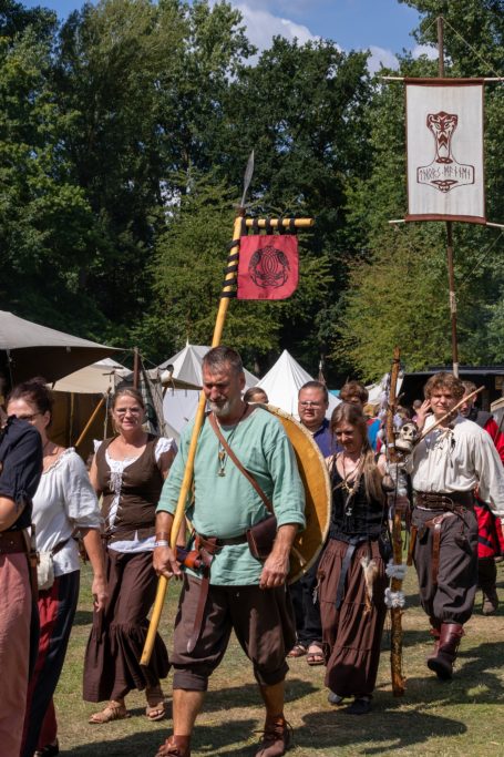 Mittelalterliche Gruppe in historischen Kostümen mit Standarten und Waffen im Freien.
