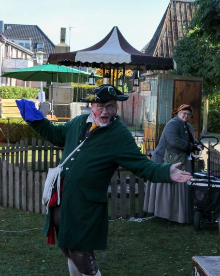 Ein Mann in historischen Kleidern mit Hut, gestikuliert fröhlich im Freien.