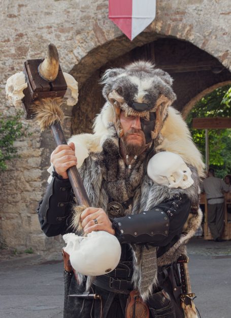 Ein kriegerartig gekleideter Mann mit einem großen Hammer und Schädeln auf der Rüstung.