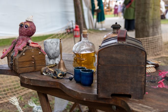 Holzkiste, Flasche, Glocke und eine Puppe auf einem Tisch im Freien.