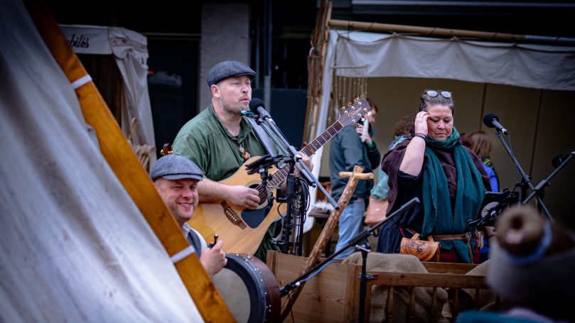 Musikgruppe spielt live auf einer Bühne, Instrumente und fröhliche Zuschauer.