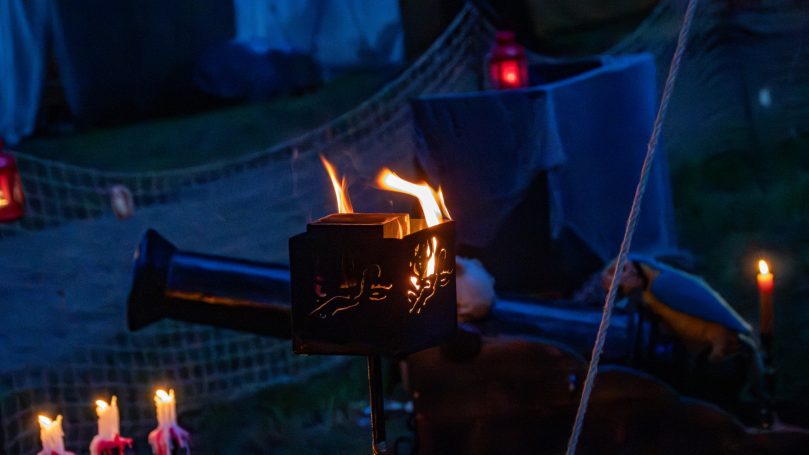 Eine Feuerstelle mit Flammen, umgeben von Kerzen und einer dunklen Kulisse.