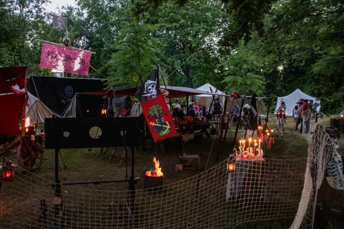 Lager mit Zelten, Fahnen und Lagerfeuer in einem Waldgebiet.