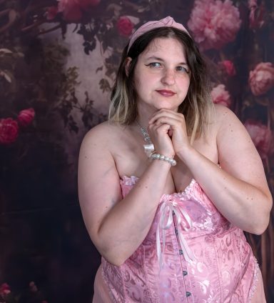 Junge Frau in rosa Kleid mit Stirnband, posiert vor blühendem Hintergrund.