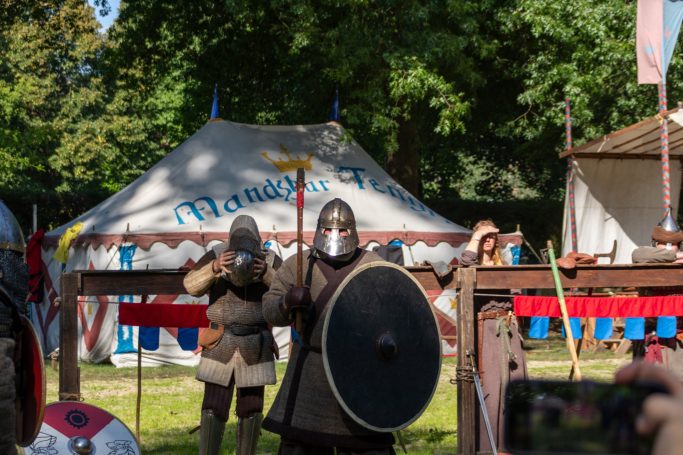 Mittelalterliche Krieger in Rüstung mit Schild und Schwert vor einem historischen Zelt.