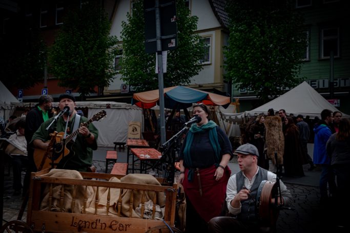 Mittelalterlicher Markt mit Musikern, Ständen und einer festlichen Atmosphäre.