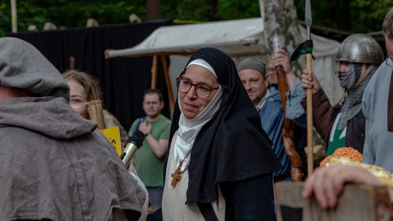 Mittelalterliche Darstellung mit Mönch und Zuschauern in historischen Kostümen.