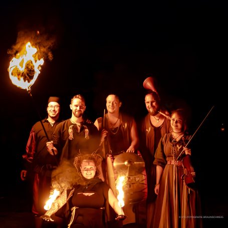Gruppe von Menschen in historischen Kostümen mit Feuer und Musikinstrumenten.