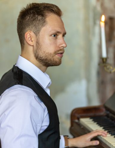 Mann mit Bart spielt Klavier, Kerze im Hintergrund.