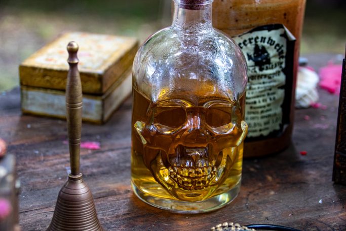 Skullförmige Flasche mit goldfarbenem Inhalt, umgeben von Gegenständen.