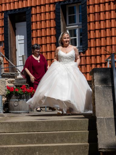 Eine Braut in einem weißen Kleid, die Stufen hinuntergeht, begleitet von einer Frau.