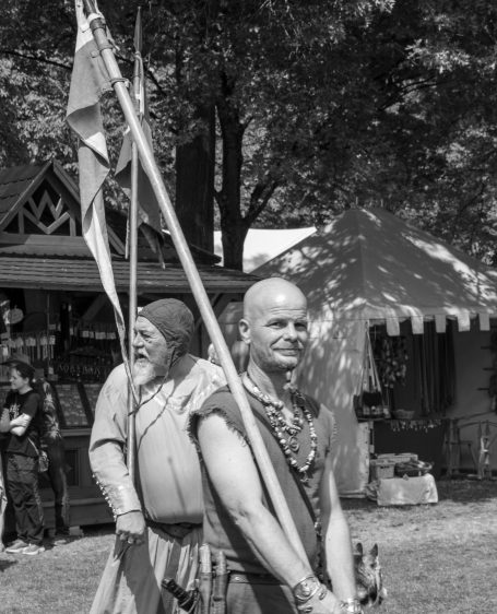 Zwei Männer in historischer Kleidung, einer hält eine Flagge, im Freien.