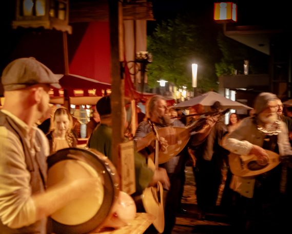 Gruppenspieler mit traditionellen Musikinstrumenten auf einem festlichen Abendmarkt.