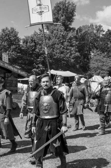 Mittelalterliche Gruppe mit Rüstungen, Fahne und Schwert in ländlicher Umgebung.