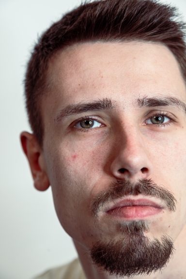 Porträt eines Mannes mit kurz geschnittenem Haar und einem nachdenklichen Ausdruck.