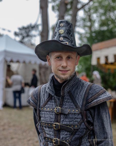 Mann in historischer Kleidung mit einem hohen Hut, in einer festlichen Umgebung.