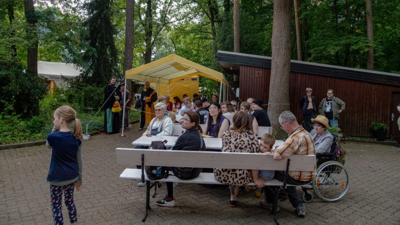 Gruppenevents im Freien mit Menschen, Bänken und einem gelben Zelt im Hintergrund.