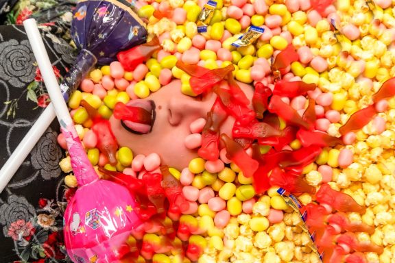 Person mit freudigem Gesicht, umgeben von bunten Süßigkeiten und Konfetti.