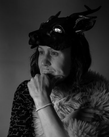 Frau in einem schemenhaften Outfit mit einem Tierkopf und nachdenklichem Ausdruck.