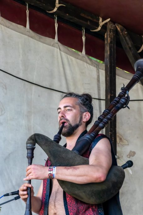 Ein Mann spielt Dudelsack auf einer Bühne, trägt ein ärmelloses Hemd.