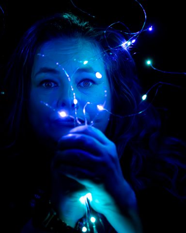 Frau mit funkelnden Lichtern in der Dunkelheit, die in ihren Händen leuchtet.