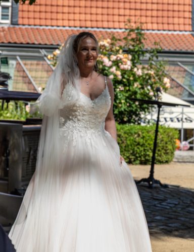 Braut in einem eleganten Hochzeitskleid mit Spitze, lächelnd im Freien.
