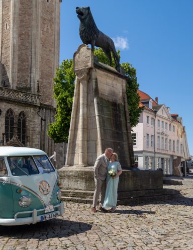 Hochzeitsfeier vor Löwendenkmal und historischem Gebäude, mit vintage Bus im Vordergrund.