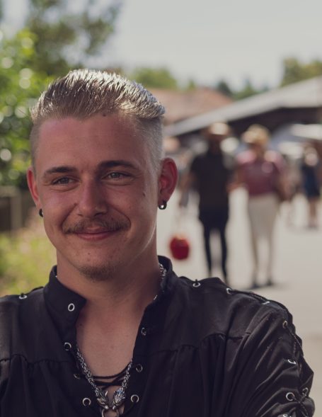 Lächelnder Mann mit kurzem, grauem Haar und Bart, im Hintergrund Menschenmengen.